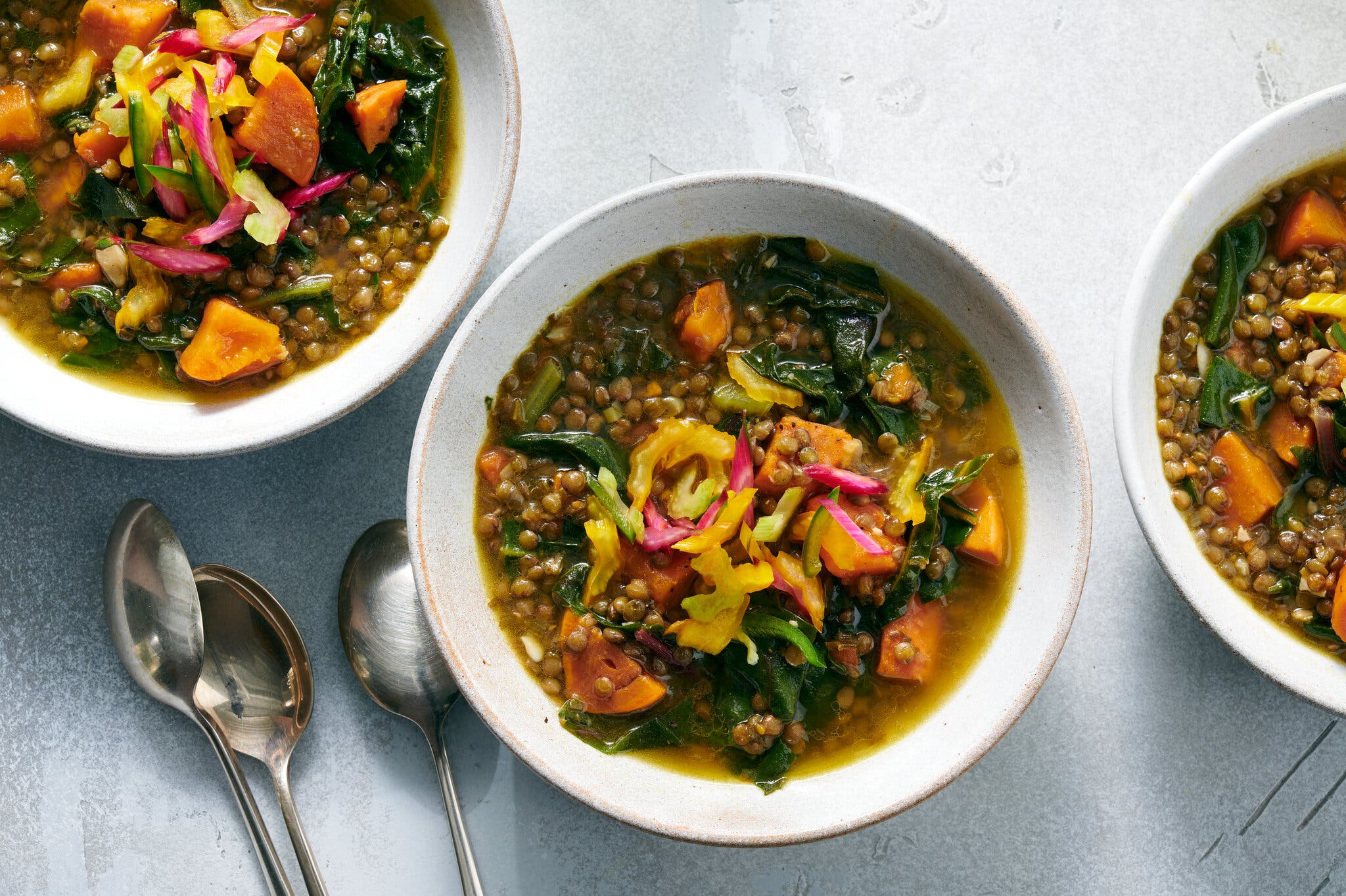 An overhead image of three bowls of lentil soup, dotted with cubed sweet potatoes.