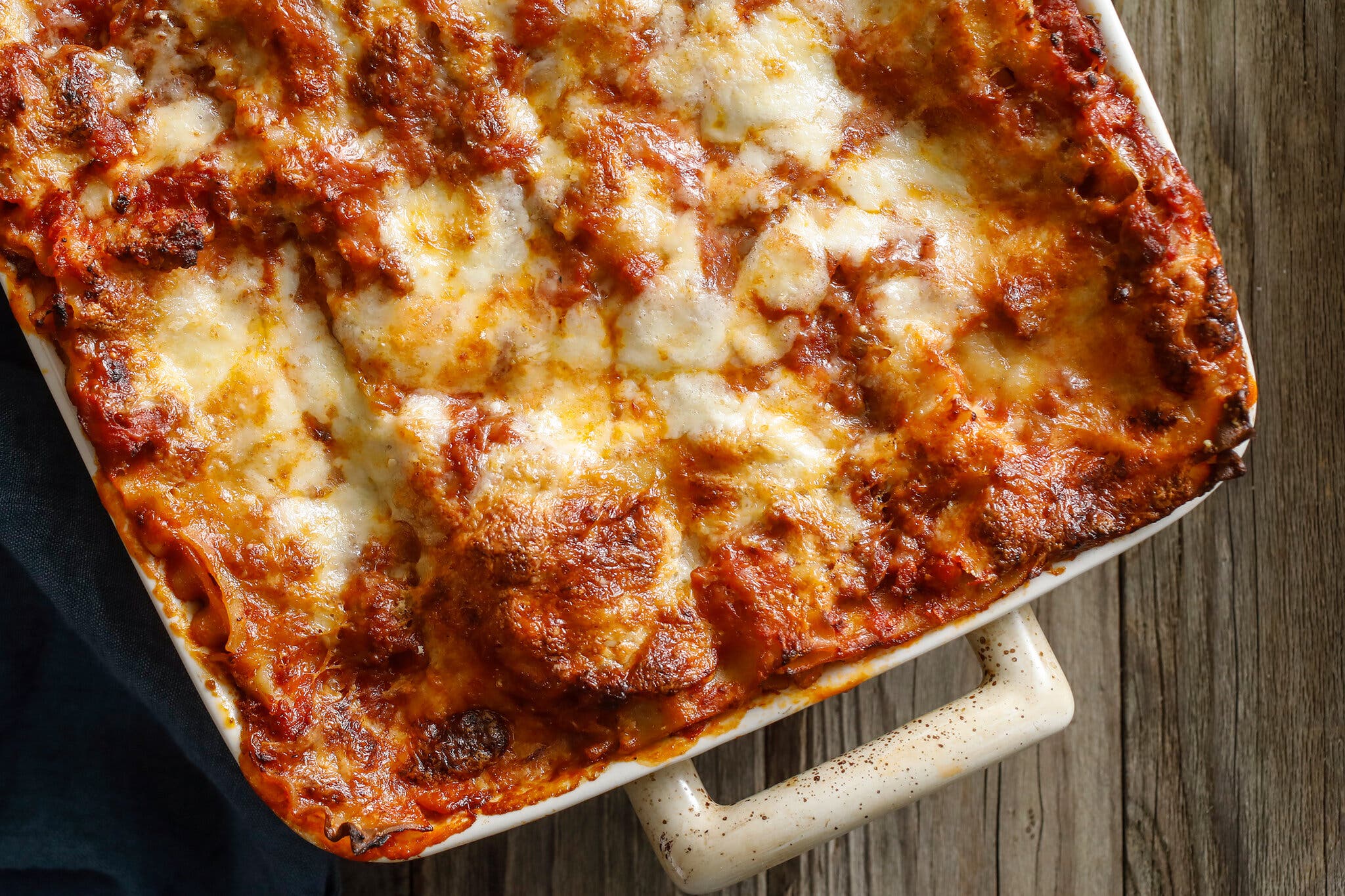 A cheesy lasagna with crisp edges is photographed from overhead on a wooden surface.