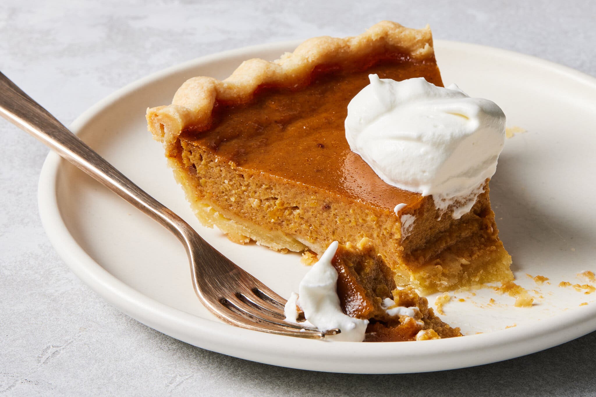 A side image of a slice of pumpkin pie with a single bite removed.