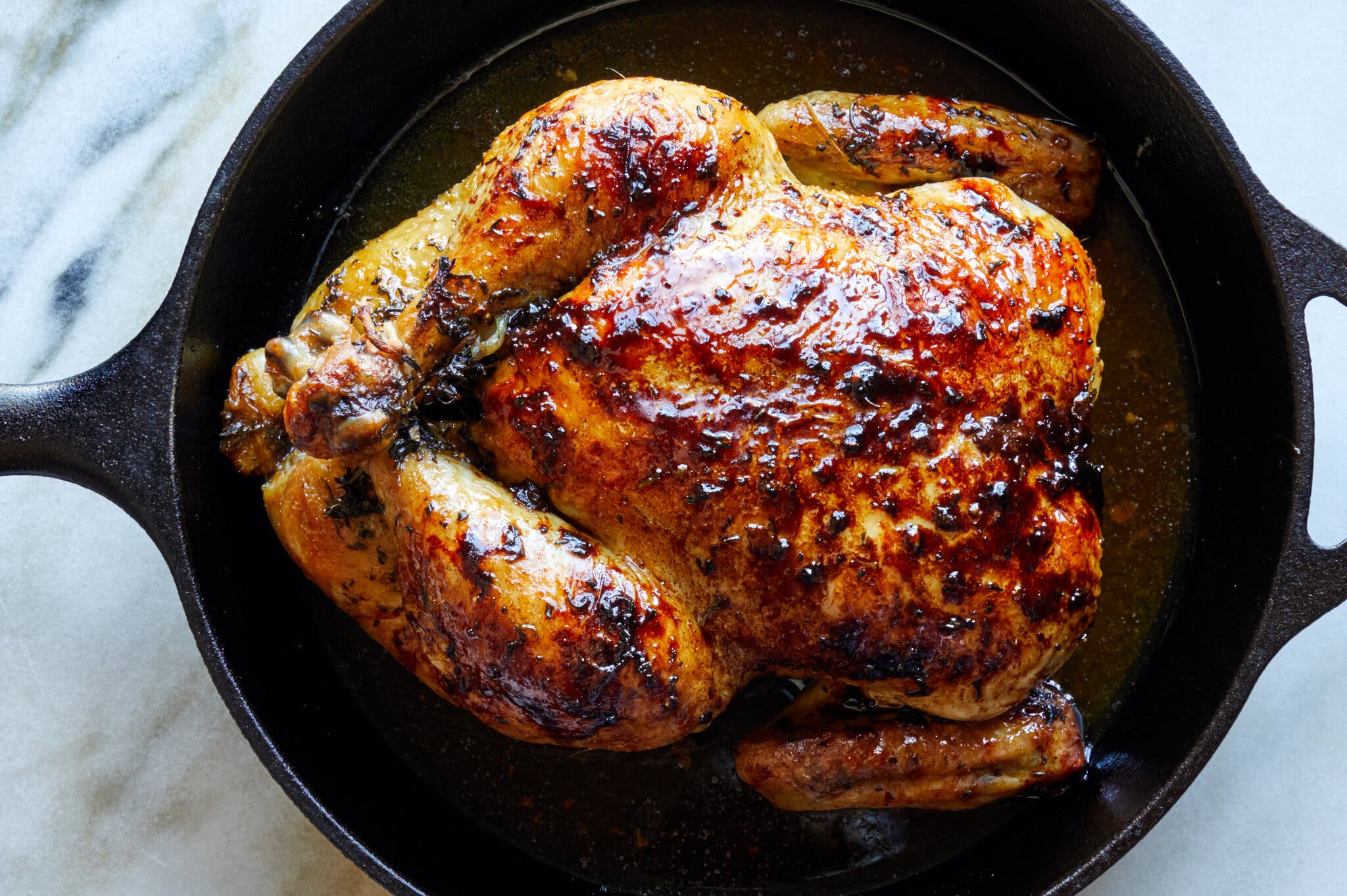 A whole burnished chicken in a cast-iron skillet is photographed from overhead.