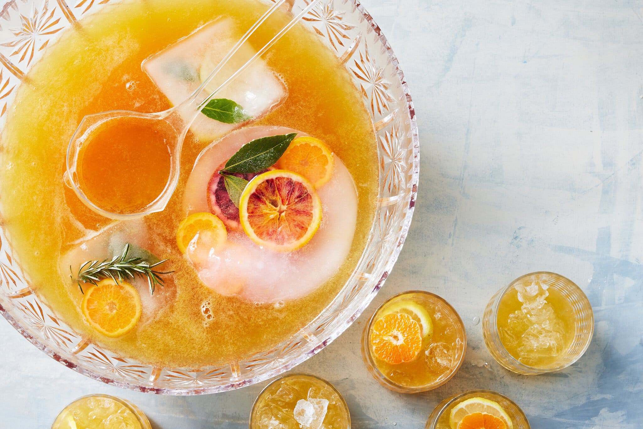 An overhead image of a punch bowl filled with a golden punch and orange slices, next to a number of smaller servings.