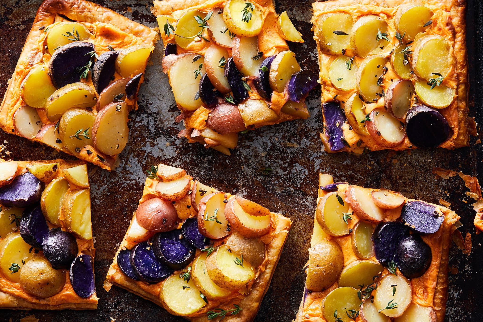 Sliced potatoes top squares of puff pastry on a sheet pan.